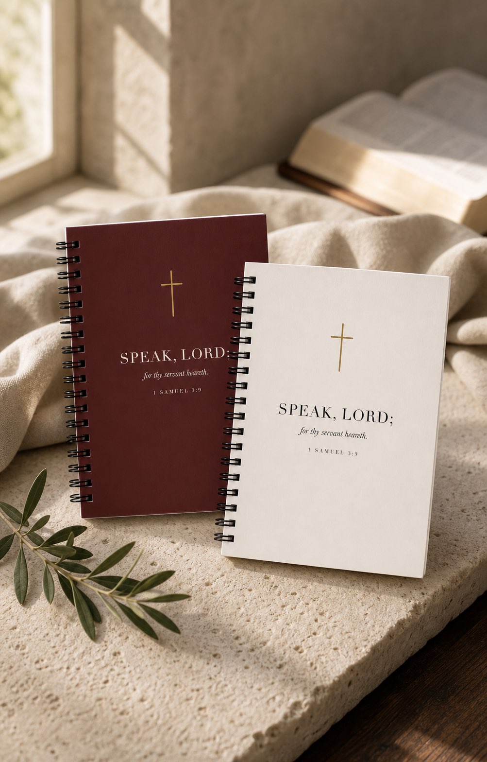 Two spiral scripture journals, oxblood and cream, resting on a stone ledge.